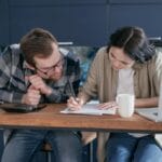 Para przy kuchennym stole analizuje dokumenty finansowe z laptopem