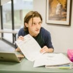 Uczeń przy biurku z laptopem i notatkami przygotowuje się do matury