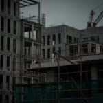 Szkielet stalowy, żelbet, prefabrykaty – porównanie popularnych technologii w inwestycjach mieszkaniowych Budowa wielorodzinnego budynku żelbetowego z żurawiem i rusztowaniami